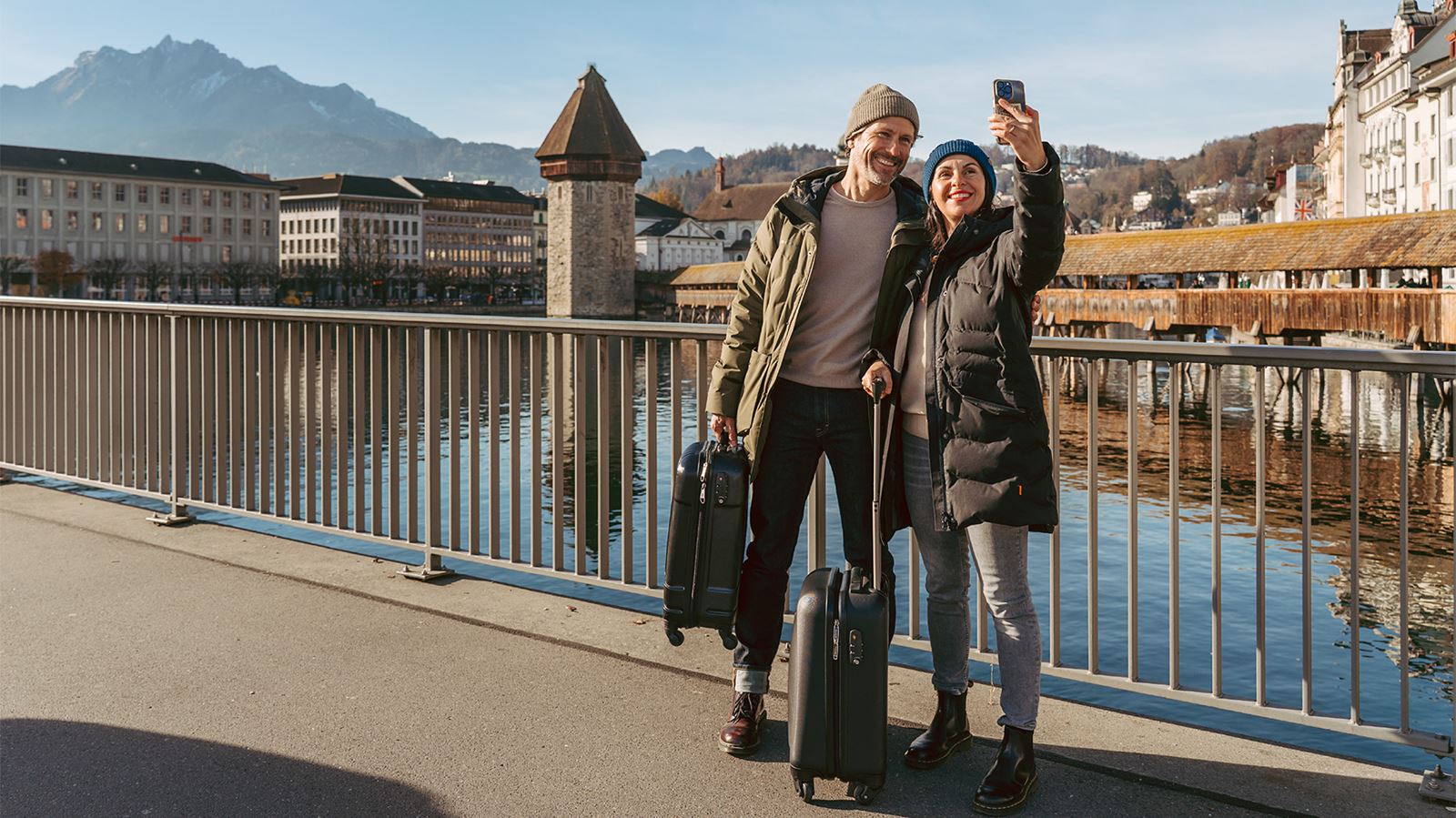 Ein reisendes Paar mit Koffern steht auf der Fussgängerbrücke in Luzern, im Hintergrund die Kapellbrücke.