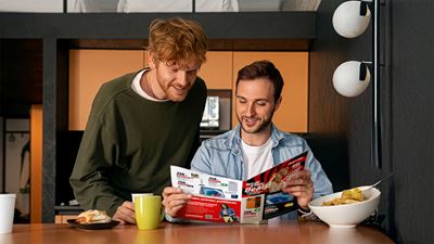 Zwei junge Männer studieren einen Produktkatalog von MediaMarkt am Frühstückstisch.